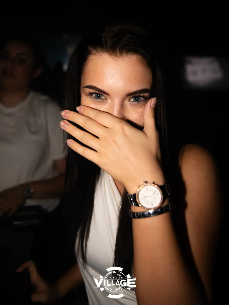 Mlada žena duge tamne kose pokriva usta rukom, nosi ručni sat, Club Village