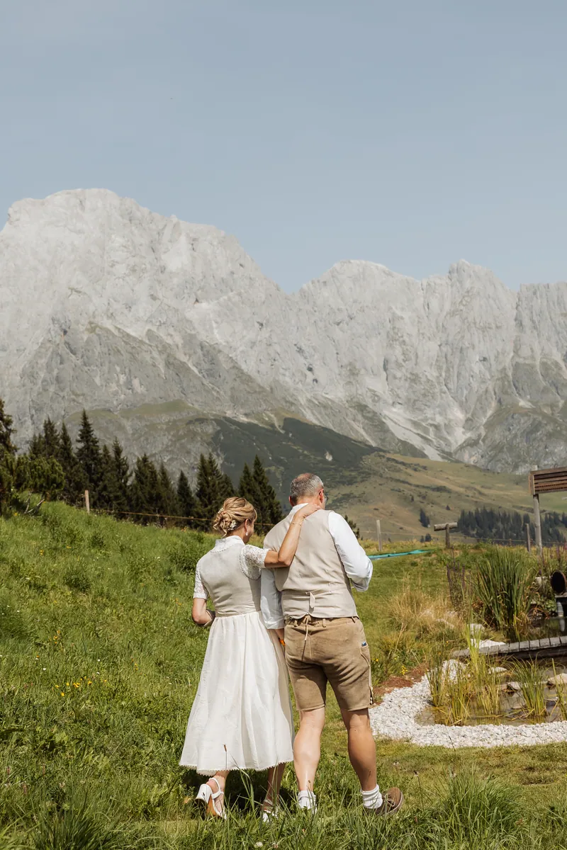 Bračni par u tradicionalnoj nošnji šeta ruku pod ruku livadom ispred stenovitih planina