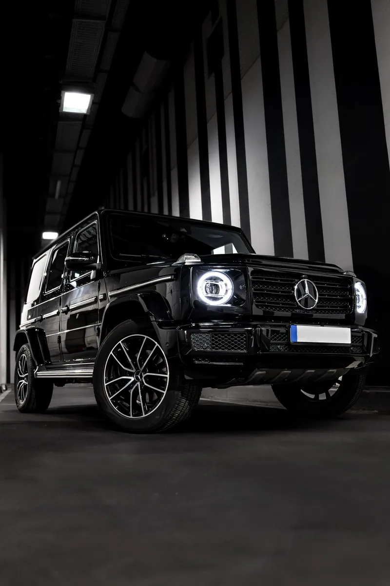Crni Mercedes-Benz G-klase sa upaljenim farovima u garaži sa crno-belim prugastim zidovima