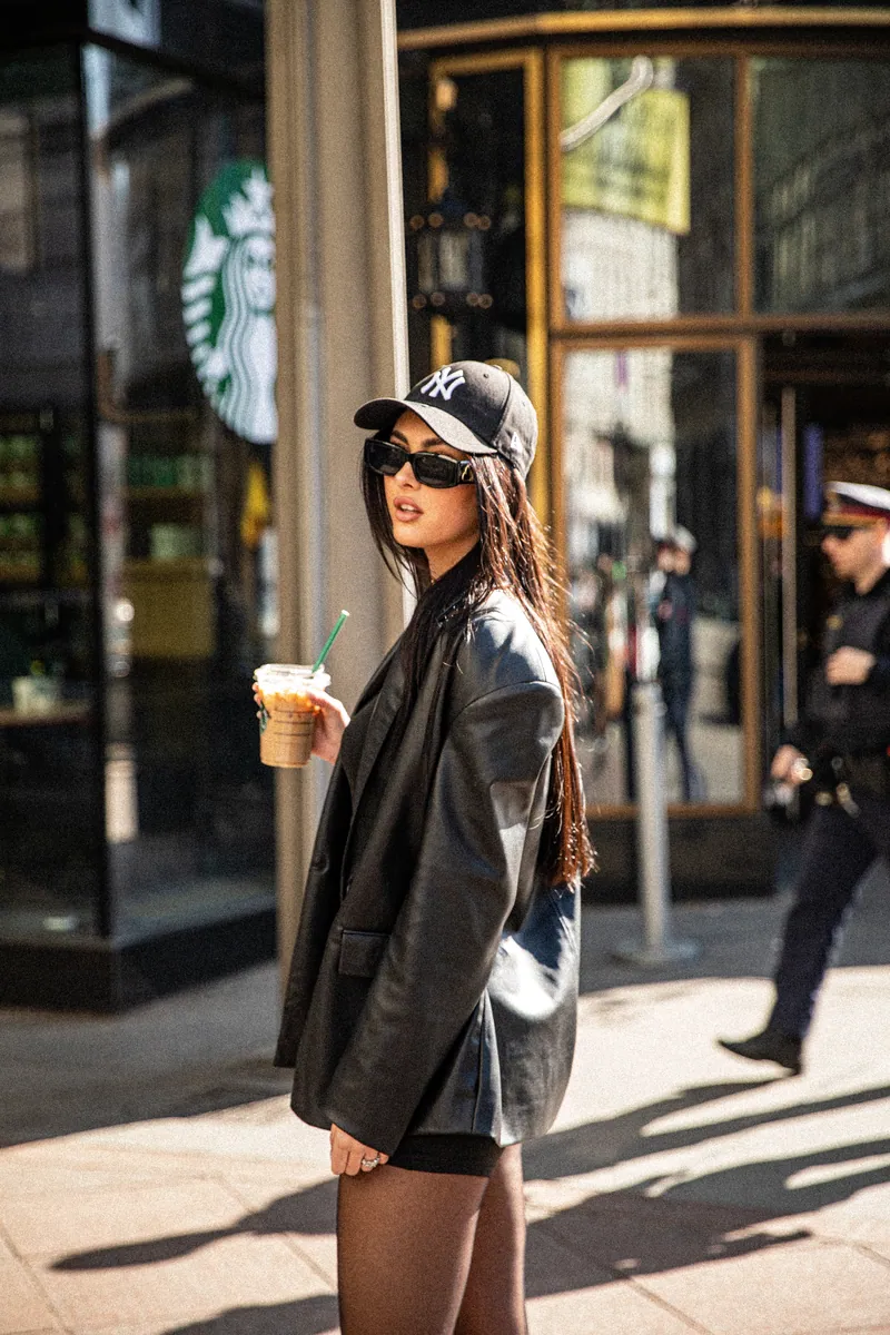 Žena sa Yankees kapom i naočarima za sunce drži ledenu kafu ispred Starbucks logotipa